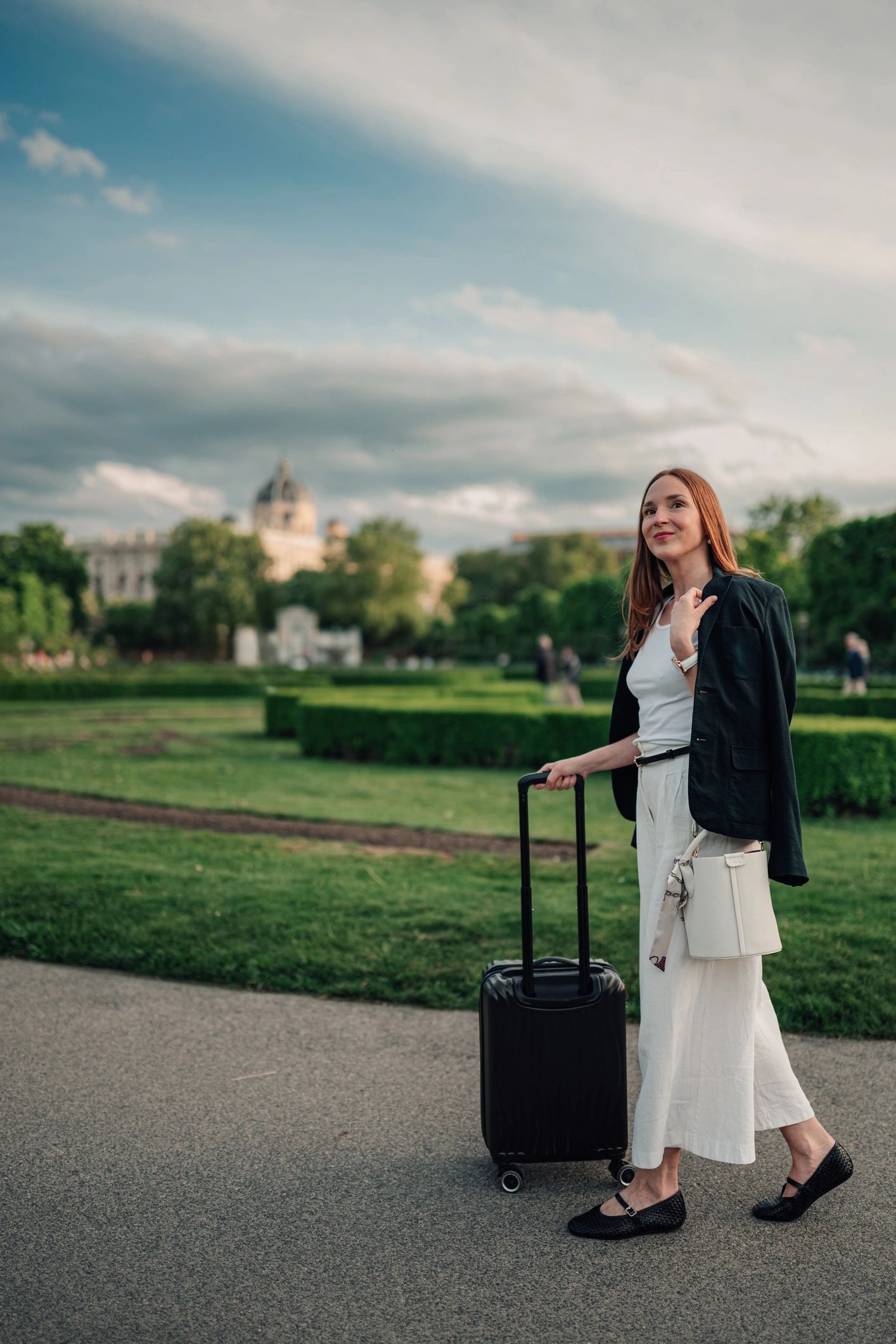 Woman pulling a suitcase in a european city park, enjoying her summer vacation and exploring the outdoors